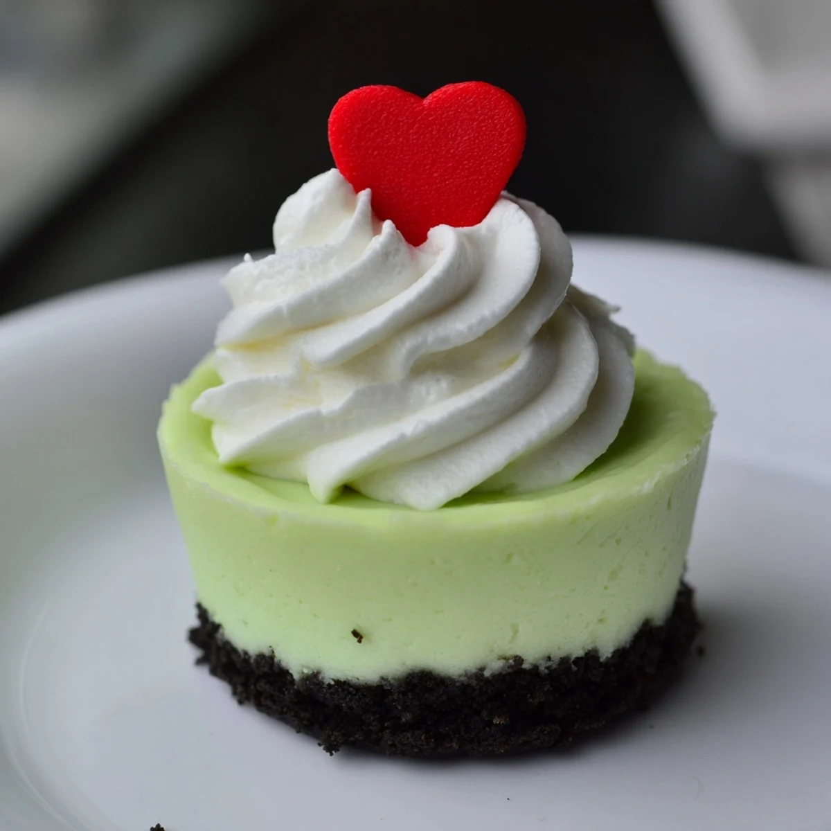 Bright green Grinch Mini Cheesecakes, topped with whipped cream and red heart sprinkles, ready to serve.