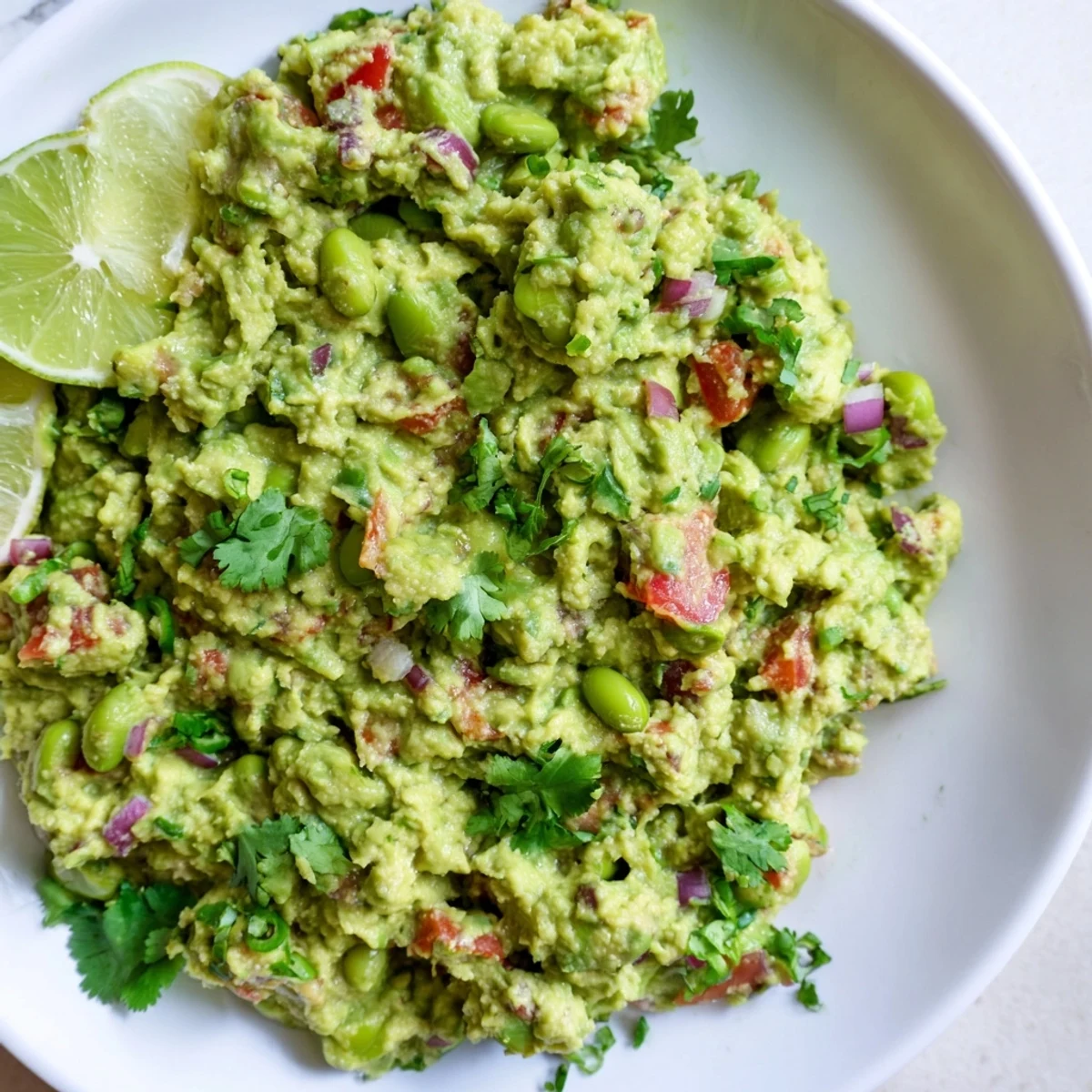 Freshly made Edamame Guacamole, with chunks of red onion and tomato, ready to be scooped up.