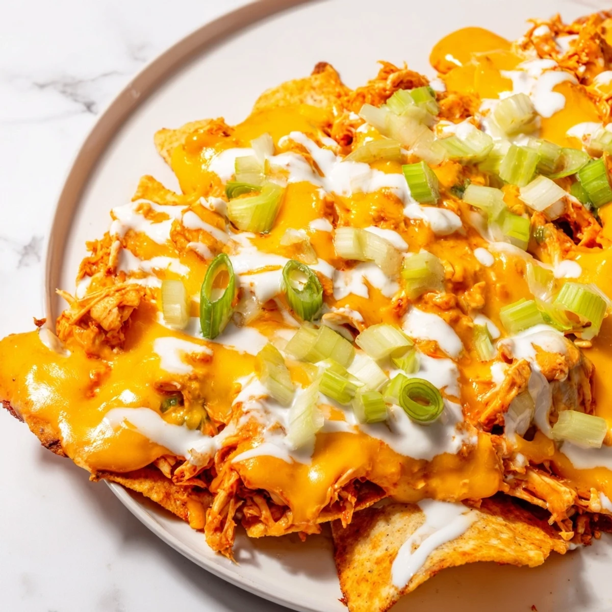 Golden-brown Buffalo Chicken Nachos topped with melted cheese, fresh green onions, and a cool ranch drizzle on a rustic serving platter.  