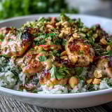 Sliced chicken and crisp vegetables drizzled with creamy Thai-inspired peanut sauce over fluffy coconut rice in a bowl.
