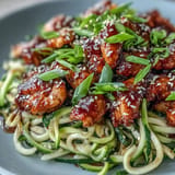 Golden honey garlic chicken surrounds al dente zucchini noodles, ready to enjoy.