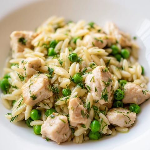 Golden-brown chicken pieces nestled in creamy orzo pasta, bright green peas, and fresh herbs in a lemony sauce.  