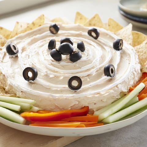 A spooky Creepy Crawly Spiderweb Platter showcases a creamy dip with olive spiders and fresh veggie dippers.