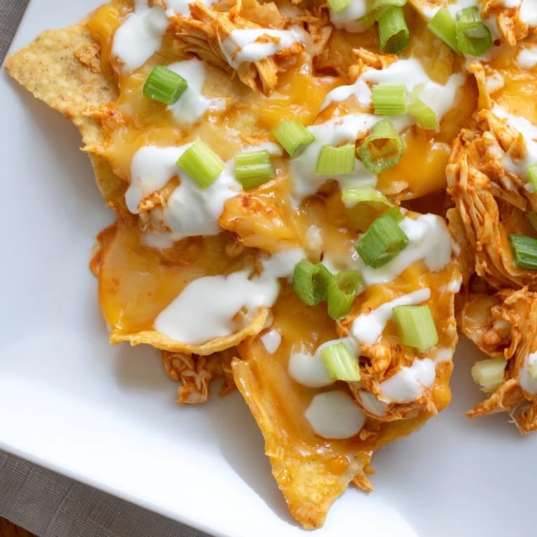 Spicy buffalo chicken and bubbling cheddar cheese layered over crispy tortilla chips, ready for game day snacking.  